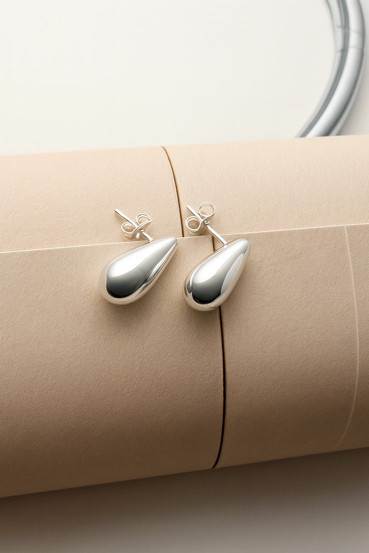 silverörhängen med droppar placerade på en ihoprullat beige tidning