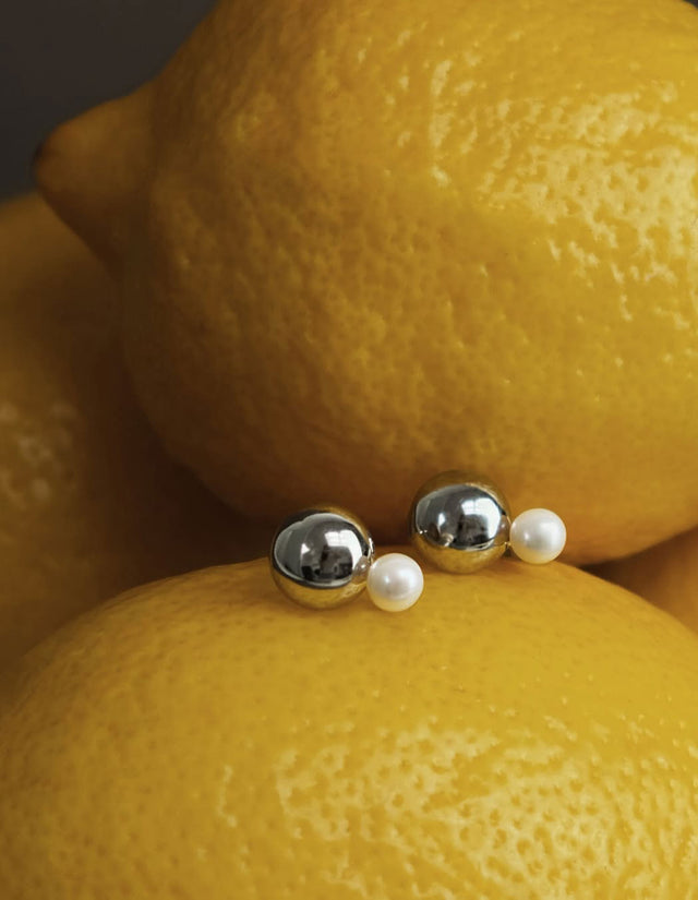 Pärlörhängen med kulor i silver placerade på två citroner. 