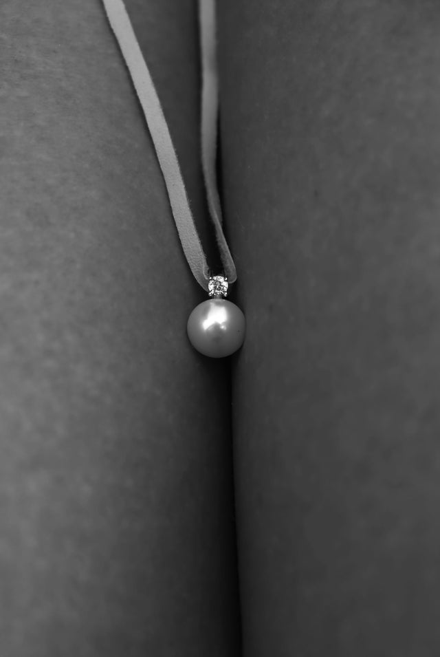 Liten vit pärla med gnistrande sten i läderband. 