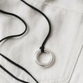 Halsband med silverring i svart läderband, placerade på vita jeans. 