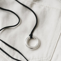 Halsband med silverring i svart läderband, placerade på vita jeans. 