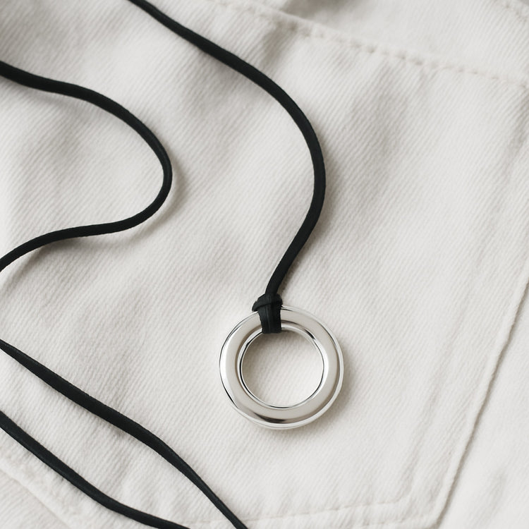 Halsband med silverring i svart läderband, placerade på vita jeans. 