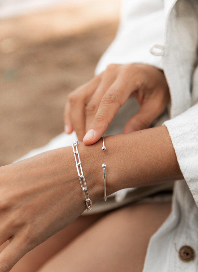 Tjej som bär silverarmband med kedja i kombination med ett smalt silver bangle. 