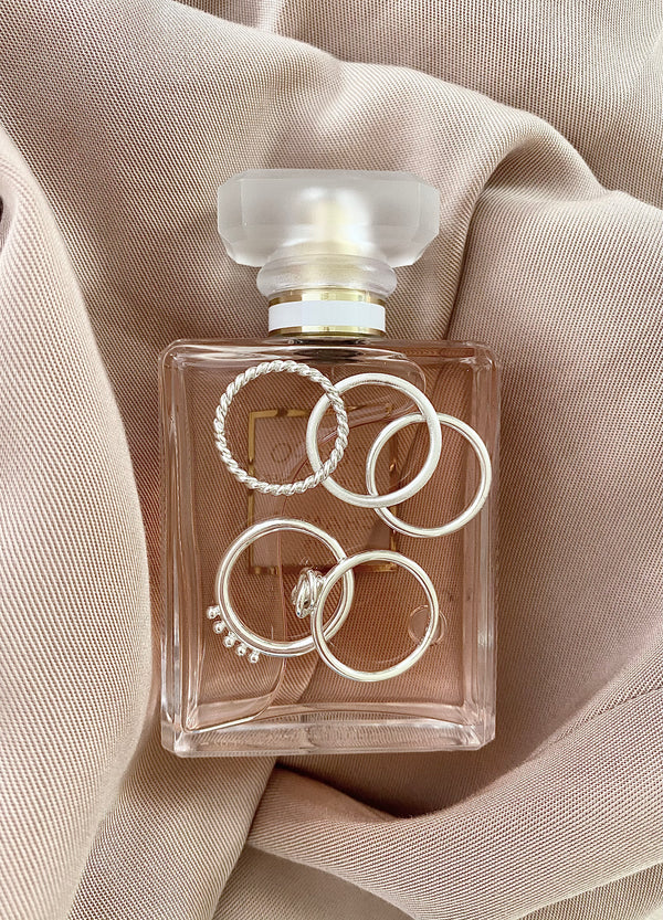 Smala silverringar som är placerade på en parfymflaska inlindad i tyg.