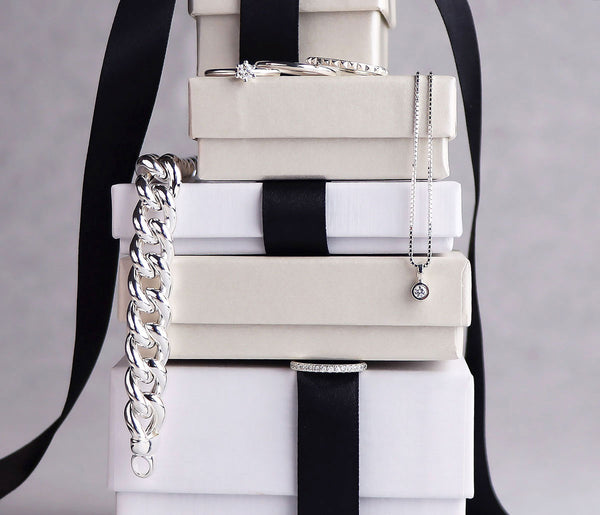 Stapel med askar i vitt och beige med silversmycken som hänger ut från askarna. 